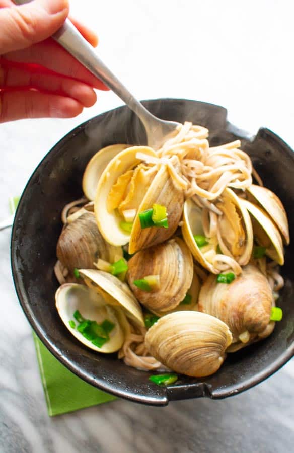 manila clams with soba noodles in black bowl