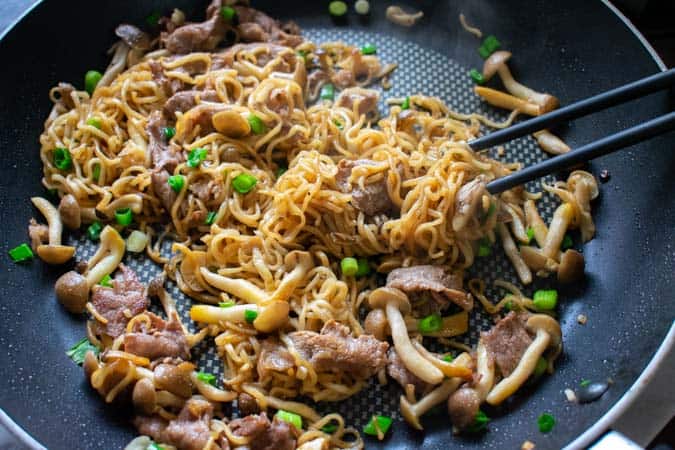 beef ramen noodle stir fry in a black nonstick pan with black chopsticks