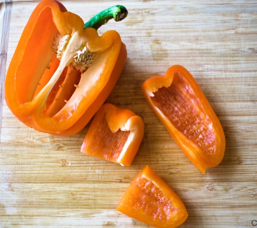 Orange bell pepper cut open on a wood cutting board. 