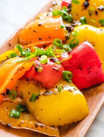 Mixed colored bell peppers with green onion on long wooden plate