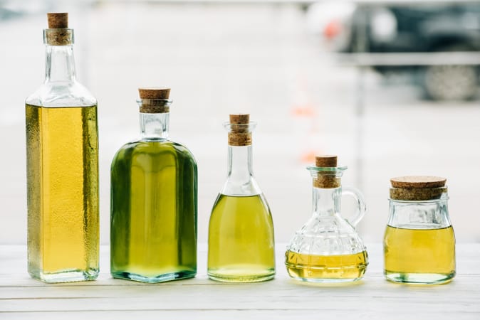 5 clear glass bottles of cooking oil in various heights and shapes, all with wooden corks.