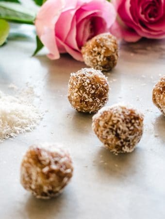 7 Coconut Date balls on marble board with 2 pink roses in the background.