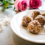 coconut date laddus on a white plate with 2 pink roses in the background
