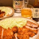 Pork tonkatsu and shredded cabbage on a plate with Asahi beer in the background.