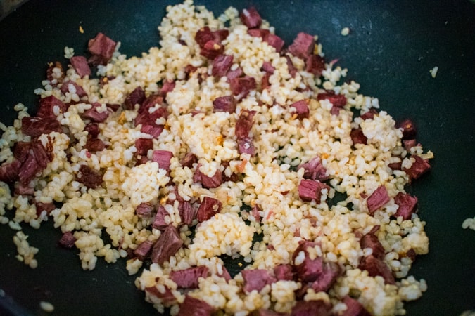 Chopped corned beef mixed with brown rice in a black wok.