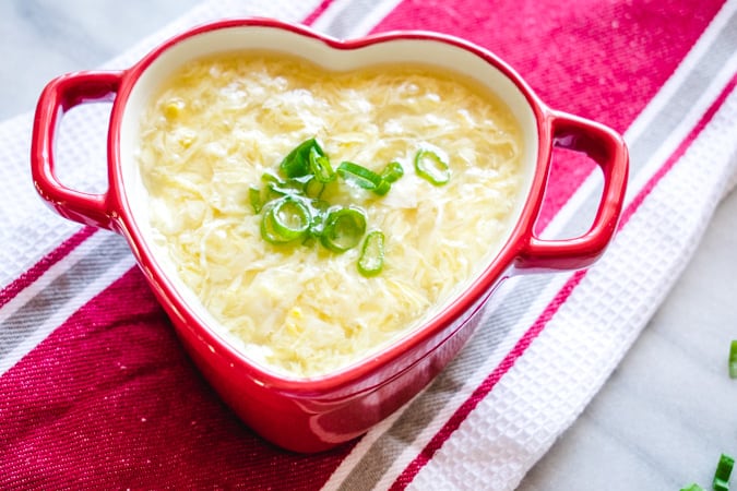 egg drop soup in a mini red heart shaped ceramic dish on a red and white striped towel