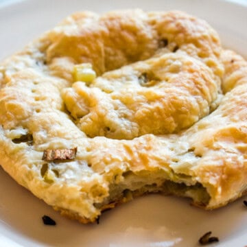 Chinese puff pastry scallion pancake with a bit taken out of it on a round white plate