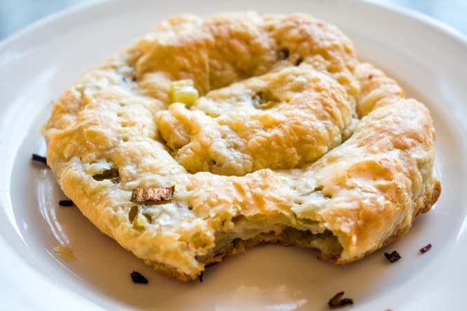 Puff pastry scallion pancake with a bite taken out of it on a white round plate
