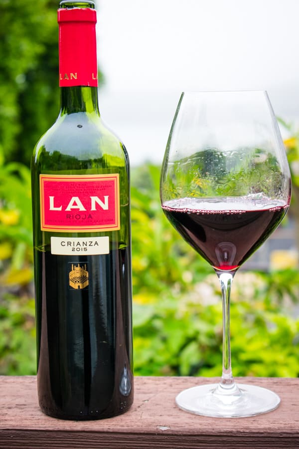 Bottle and wine glass of 2015 Bodega LAN Crianza Rioja with green plants in the background