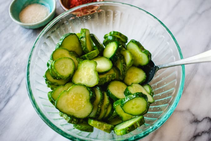 Sliced kirby cucumbers in glass bowl brining in salt.