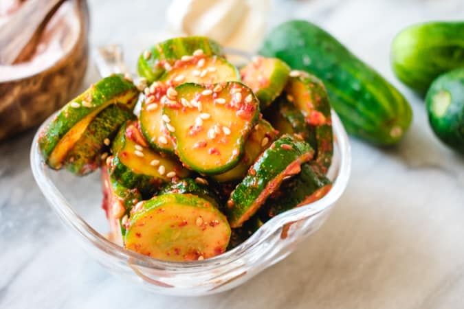Cucumber kimchi with red Korean chili flakes and sesame seeds in glass dish.