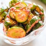 Close up shot of cucumber kimchi in glass bowl with sesame seed garnish.