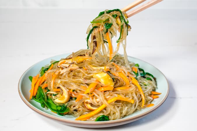 Korean vegan sweet potato noodles and vegetables with chopsticks.