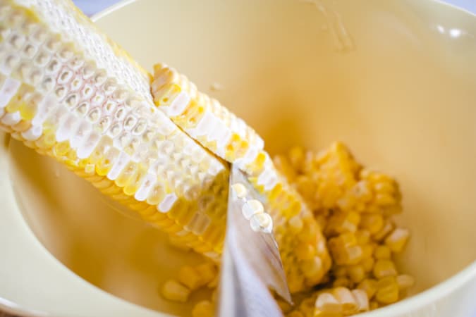 knife shaving off corn kernels into a yellow bowl