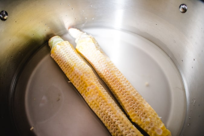 2 corn cobs in water in a stainless steel pot