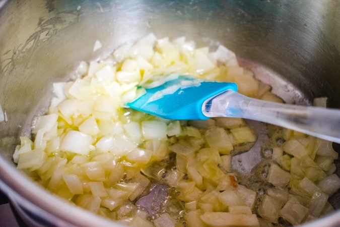 Diced onions sauteeing in a pan with a blue spatula