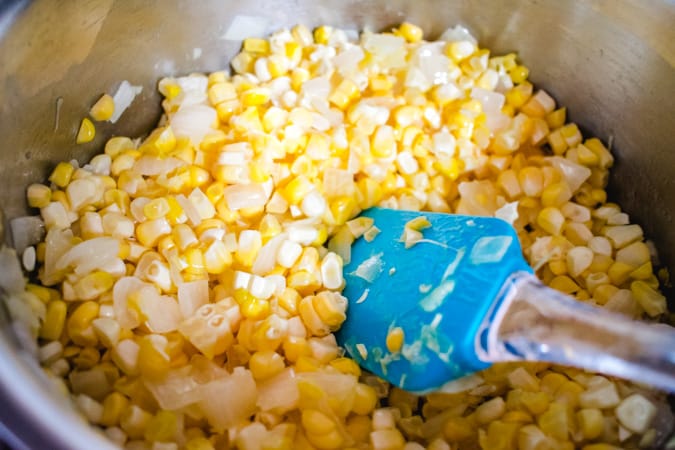 Fresh corn sauteeing in a pot with a blue spatula