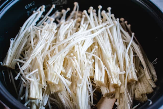 rice cooker filled with raw rice and enoki mushrooms