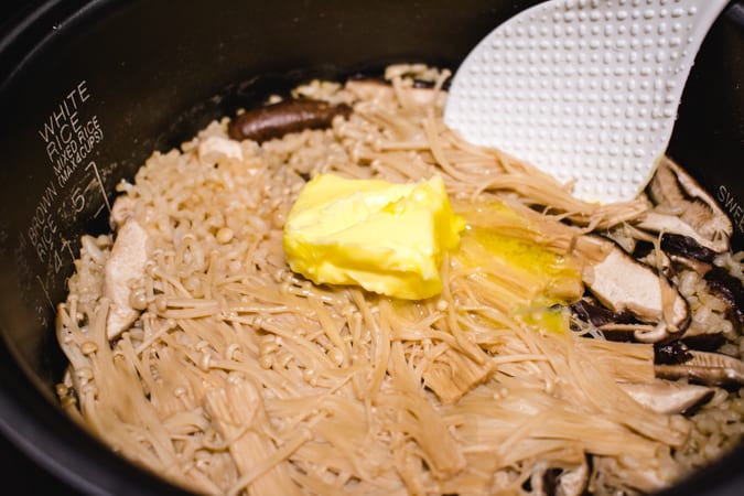 Rice cooker filled with mushroom rice, butter, and spatula