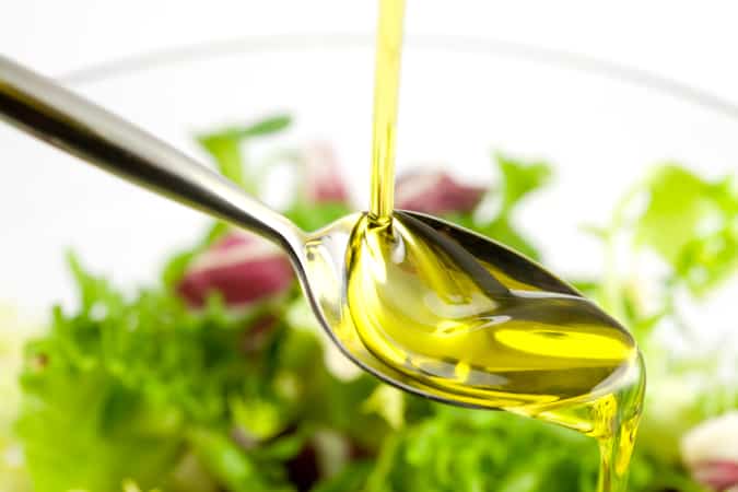 Olive oil being poured onto a spoon over a bowl of salad greens