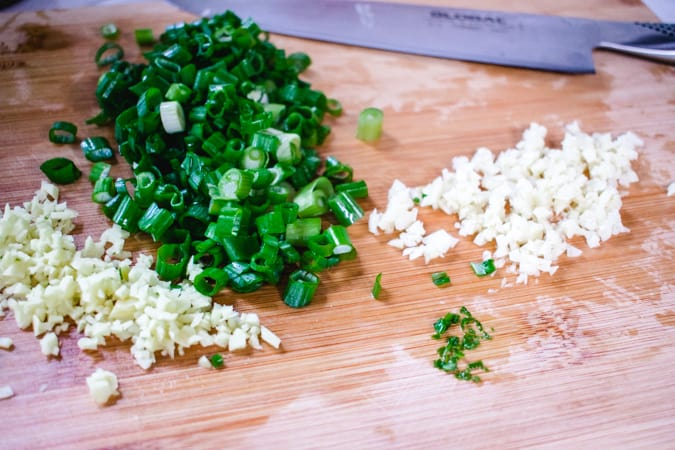 minced ginger, green onion, and garlic on cutting board with knife