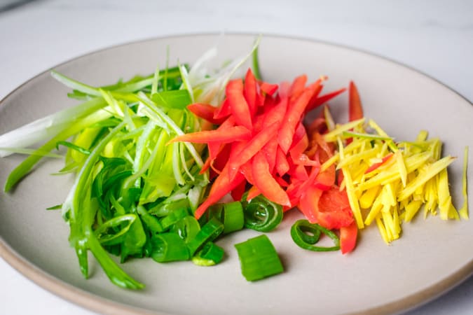 sliced green onion, red bell pepper, and ginger on a beige round plate