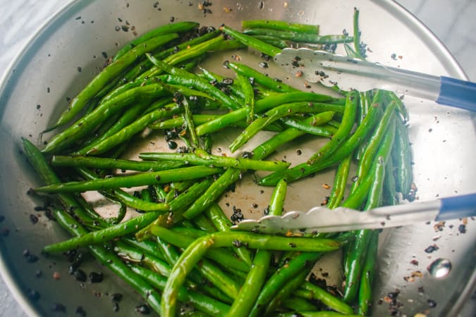 green beans with black beans in a skillet with tongs
