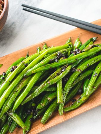 Chinese blackened green beans on wooden plate with black chopsticks