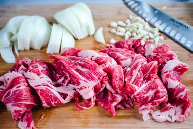 sliced beef, onion, and garlic on a wooden cutting board