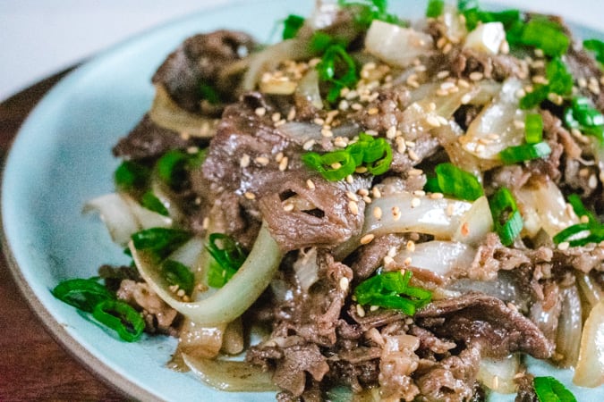 Korean bbq beef and onion with green onion on a blue plate