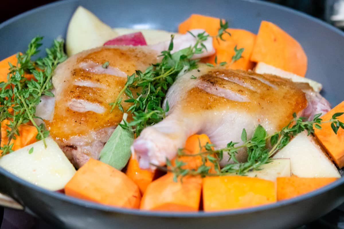 seared duck legs in skillet with sweet potatoes and thyme