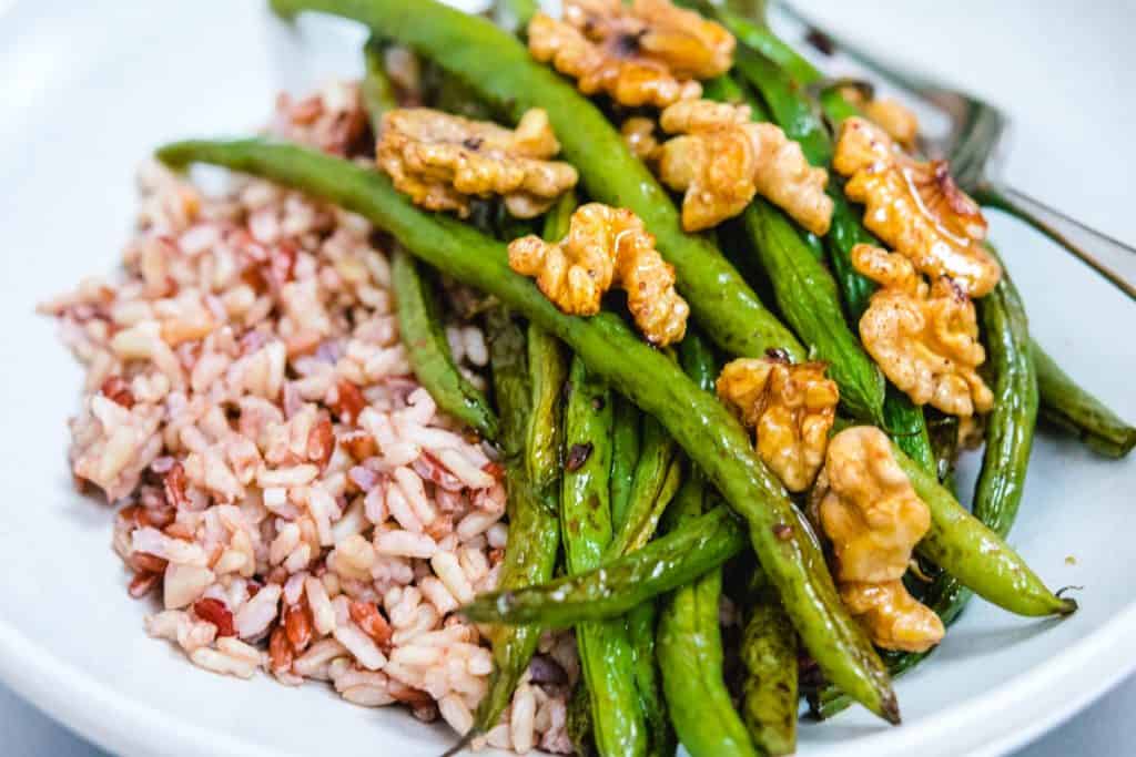 close up of roasted green beans, walnuts, and brown rice in a white bowl