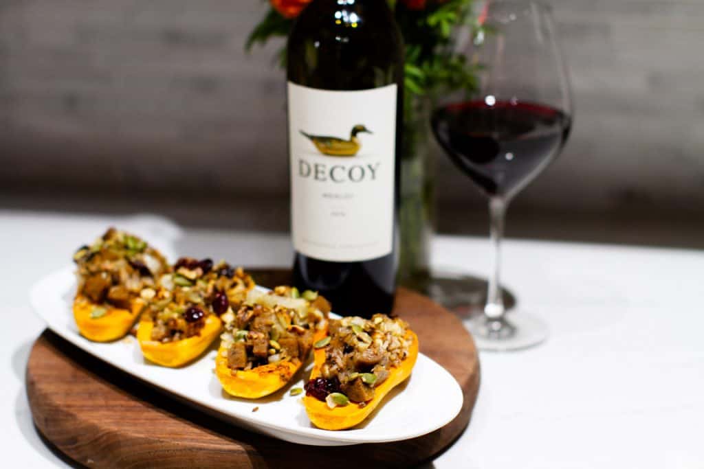 4 stuffed honeynut squash on a plate with Decoy wine in the background