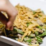 a hand putting fried onions on the green bean casserole