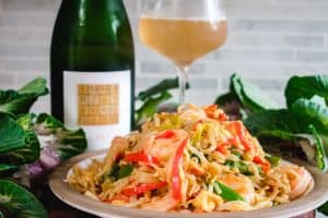 a large pile of shrimp chow fun on a plate with wine in the background