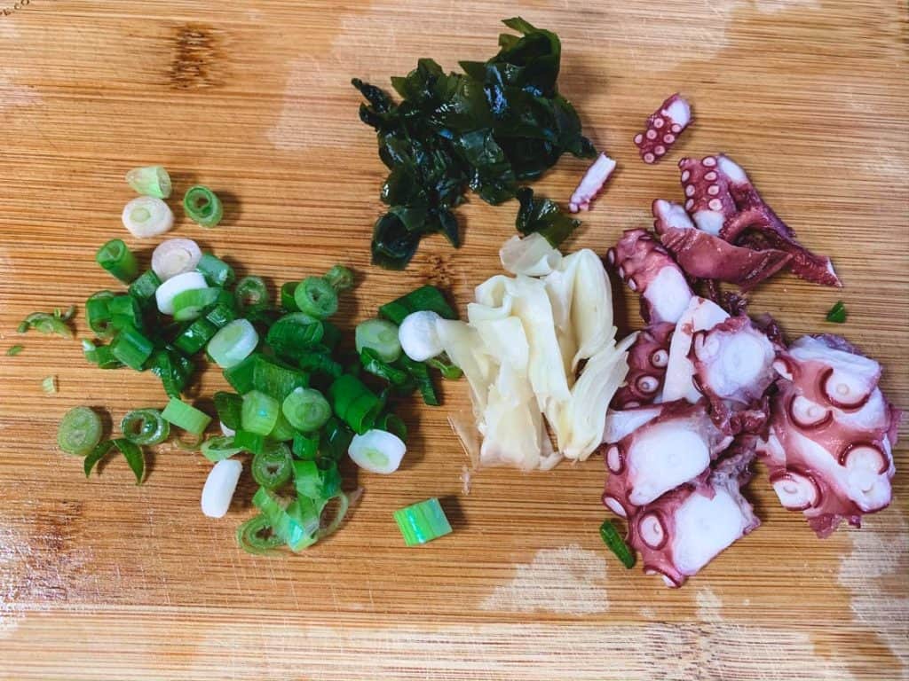 ingredients for tako poke chopped on a wooden cutting board
