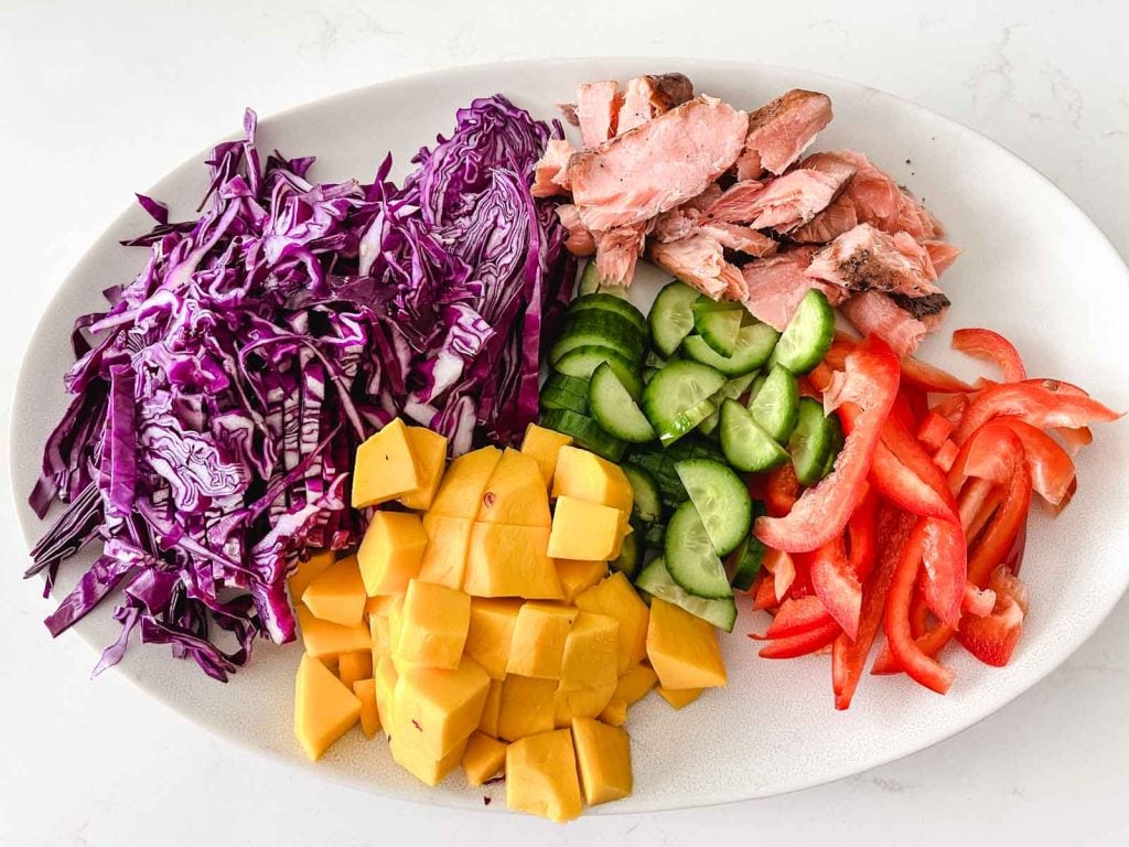prepped vegetables and salmon on an oval white plate