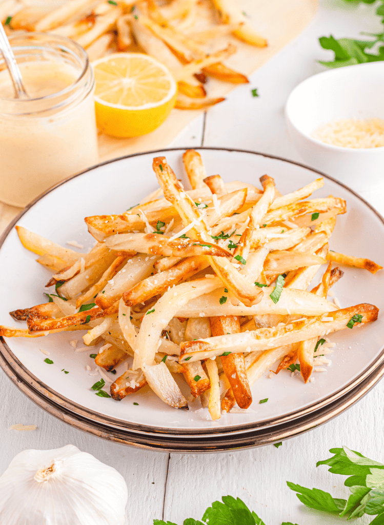 Parmesan truffle fries on a white round plate with fries in the background