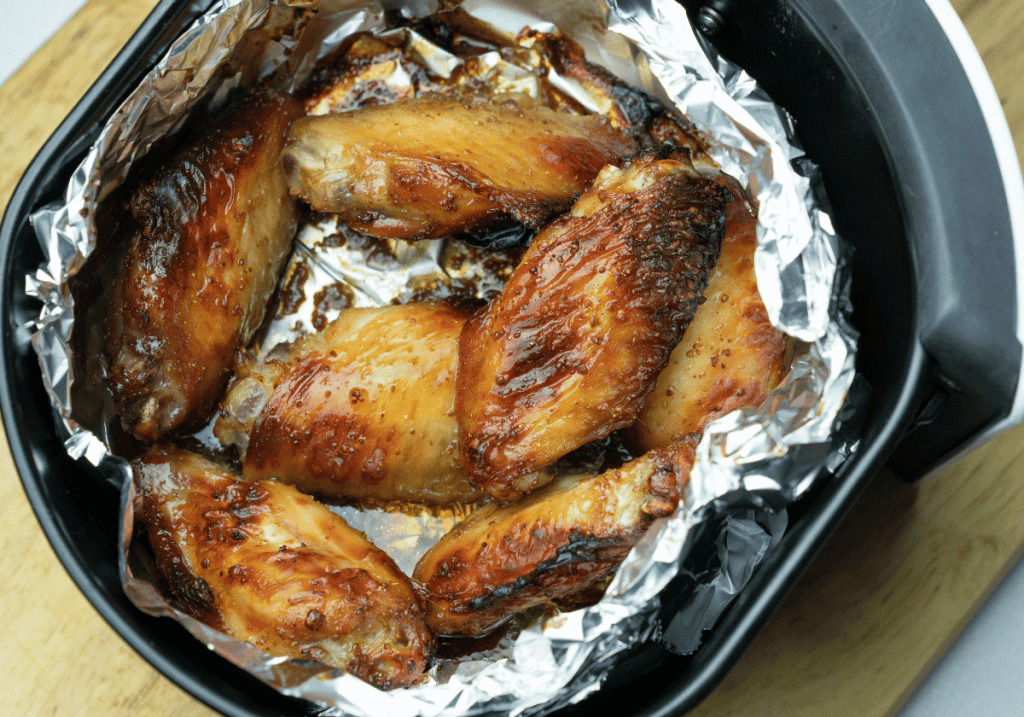browned chicken wings in foil in an air fryer basket