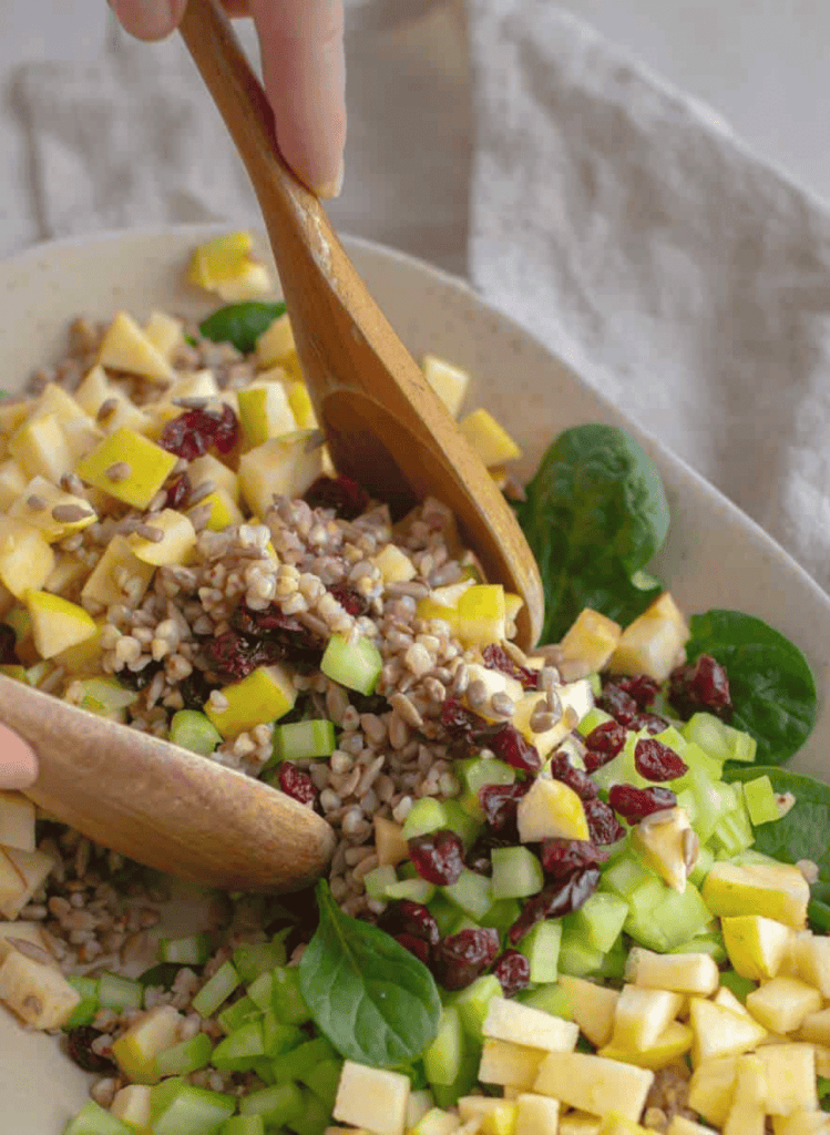 buckwheat cranberry apple salad in a white oval bowl and 2 wooden spoons