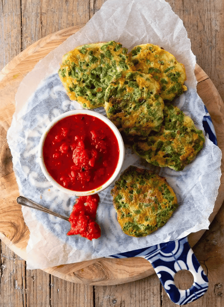 guatamalen green bean fritters on a round cutting board with a ramekin of red salsa