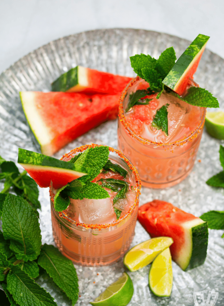 2 glasses of watermlon cocktails with watermelon slices, lime wedges, and mint leaves