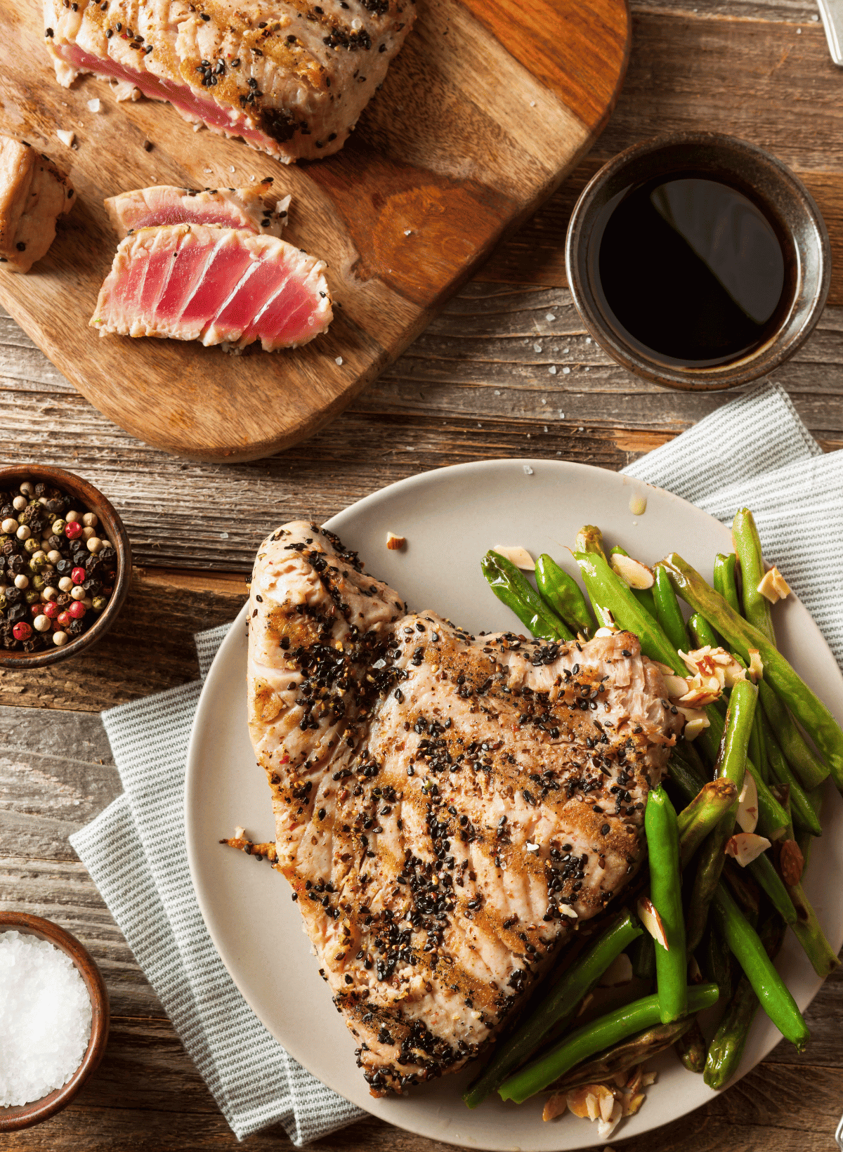 Sliced tuna steak on a wooden cutting board and a large grilled tuna steak on a white plate with green beans