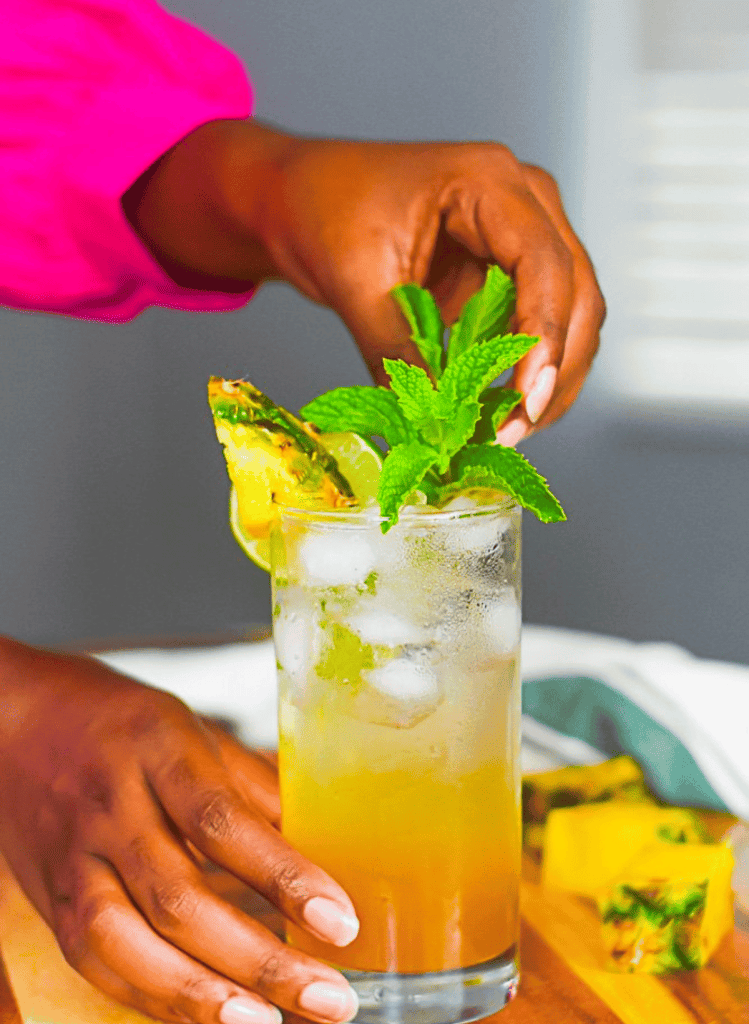 hands putting a mint garnish on a pineapple mojito in a glass