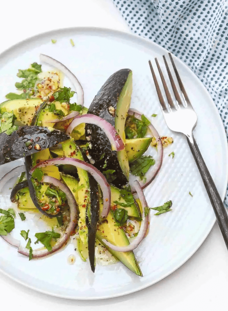 sliced avocado salad with the skin on a white round plate and a silver fork