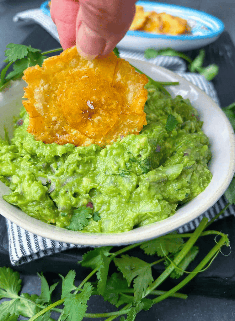 a plantain chip being dipped into a bowl of guacamole