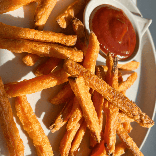 sweet potato fries on a white plate with a cat shaped ramekin of ketchup