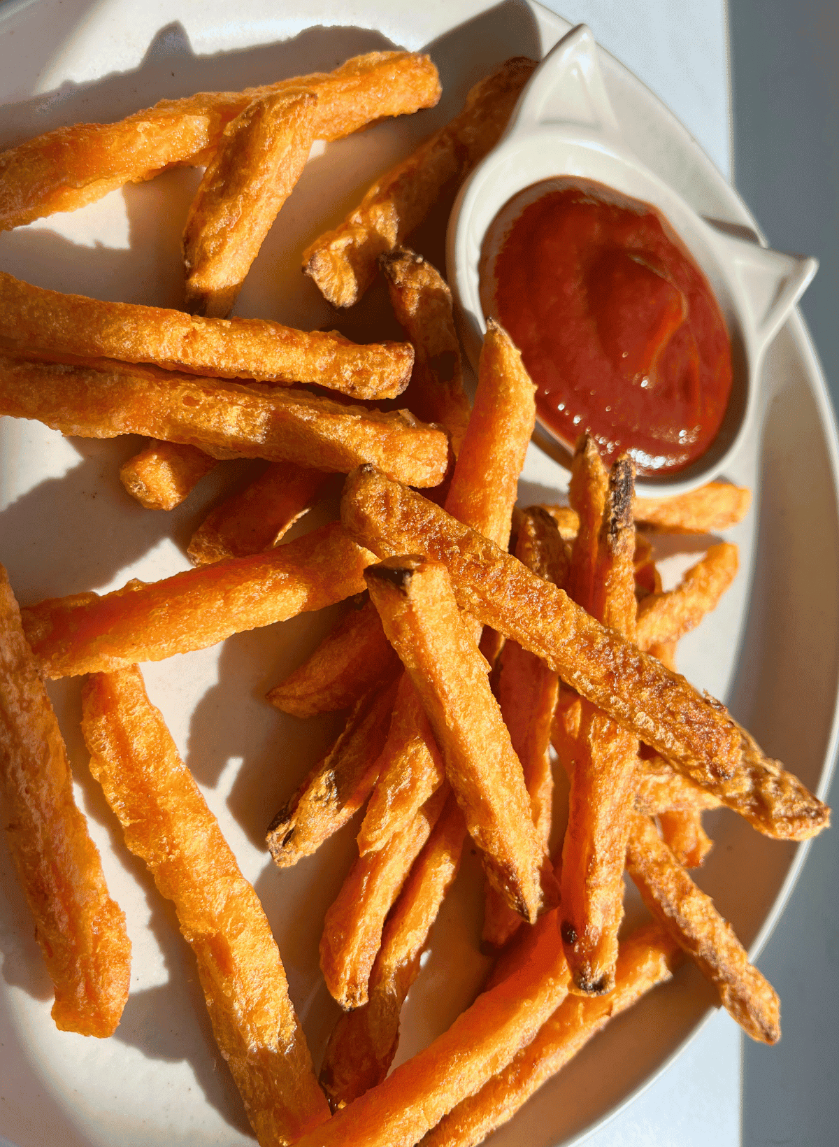 sweet potato fries on a white plate with a cat shaped ramekin of ketchup