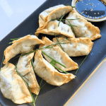 black rectangular plate of air fried gyoza with a cat shaped ramekin of soy sauce and sesame seeds