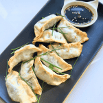 black rectangular plate of air fried gyoza with a cat shaped ramekin of soy sauce and sesame seeds